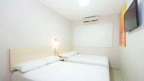 Ett hotellrum med två separata sängar, ett nattduksbord med en lampa, en väggmonterad TV och ett fönster med utsikt.