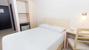 Ett enkelrum med en säng, ett sängbord med en lampa och en garderob med en spegel.