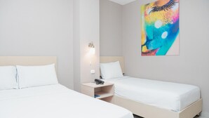 Ett hotellrum med två separata sängar, ett nattduksbord med en lampa och en färgstark, abstrakt tavla på väggen.