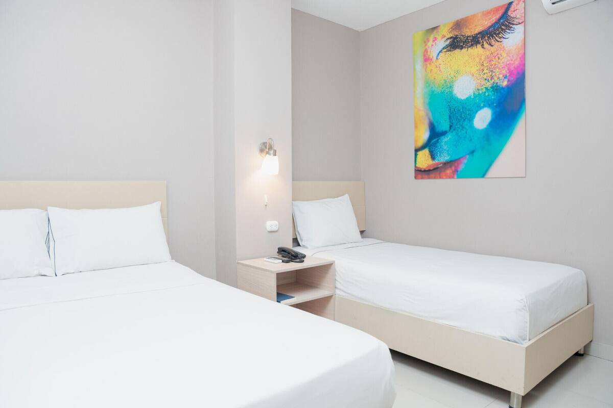 A hotel room with two single beds, a bedside table with a lamp, and a colorful abstract painting on the wall.