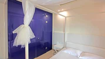 A hotel room with a bed, a bedside table, a window with curtains, and a mirror.