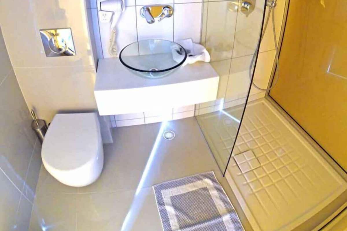 A bathroom with a glass shower enclosure, a white sink with a glass basin, and a toilet.