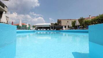 A swimming pool with lounge chairs and umbrellas, surrounded by buildings.
