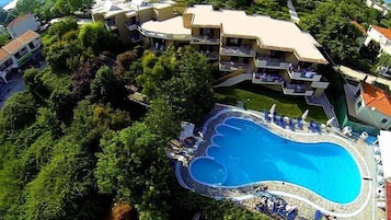 Vista aérea de un complejo turístico con piscina rodeada de exuberante vegetación y varias edificaciones.