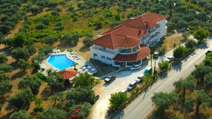 An aerial view of a multi-story building with a swimming pool, surrounded by olive trees and a road. - Achillion (Thasos)
