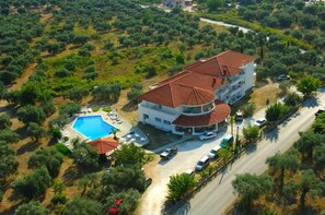 An aerial view of a multi-story building with a swimming pool, surrounded by olive trees and a road. - Achillion (Thasos)