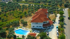 A large white building with a red-tiled roof, a swimming pool, and a parking area. - Achillion (Thasos)