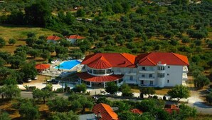 A large white building with red roofs, surrounded by greenery and trees. - Achillion (Thasos)
