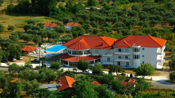 A large white building with a red roof, surrounded by trees and a swimming pool. - Achillion (Thasos)