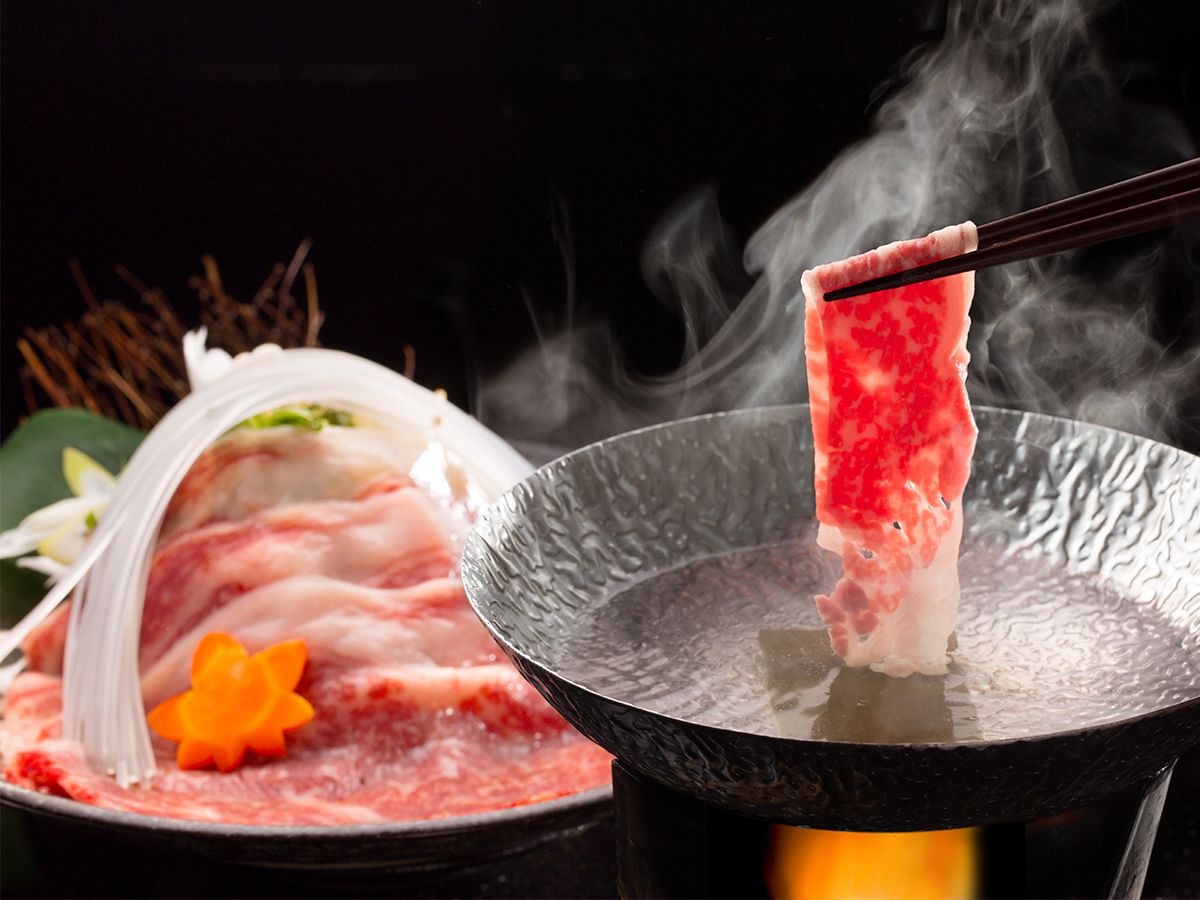 A hot pot with raw meat being cooked.
