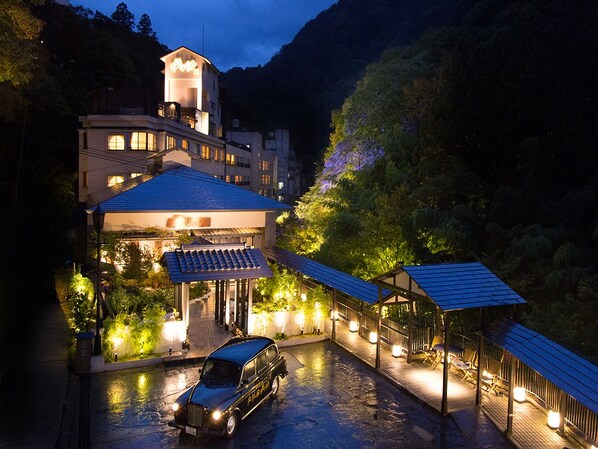 A hotel with a covered outdoor area, a car parked in front, and a mountain backdrop. - Shousuke no Yado Takinoyu (Aizuwakamatsu)