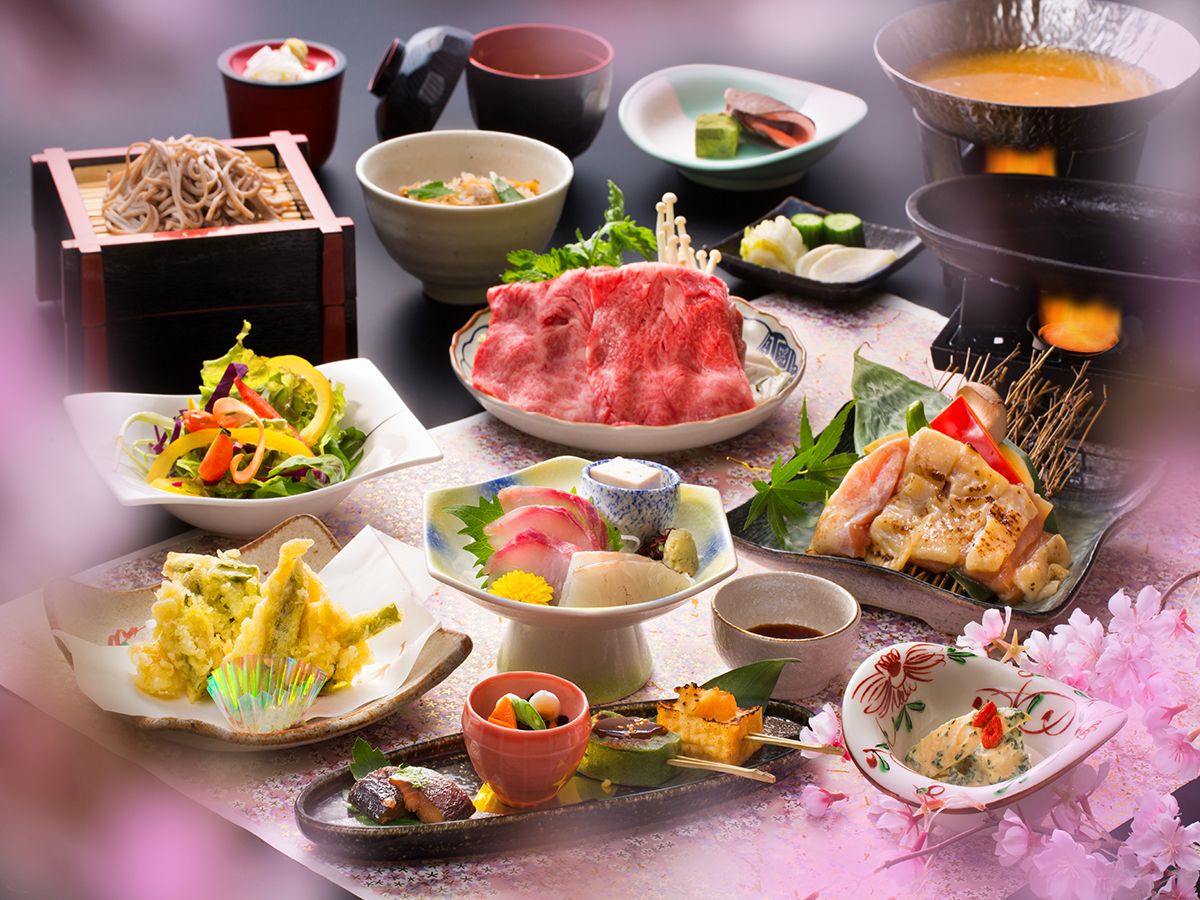 A variety of Japanese dishes including sushi, sashimi, and tempura, arranged on a table with cherry blossoms.