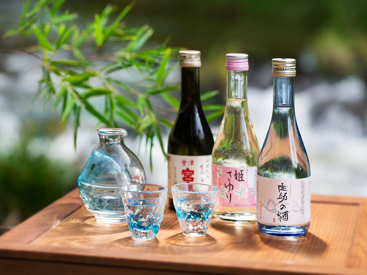 Una mesa de madera con cuatro botellas y dos vasos, presumiblemente con bebidas, sobre un fondo natural desenfocado.