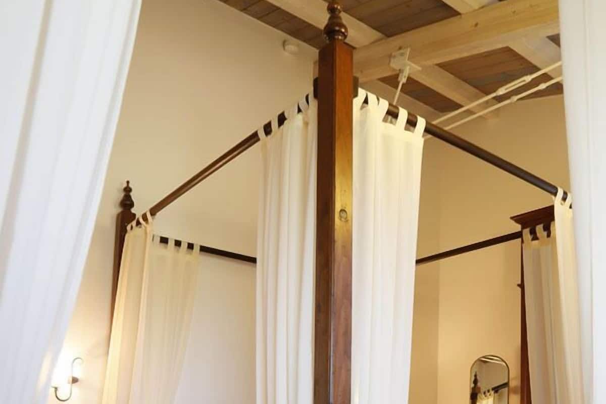 A four-poster canopy bed with white curtains, a wooden headboard, and a floral bedspread.
