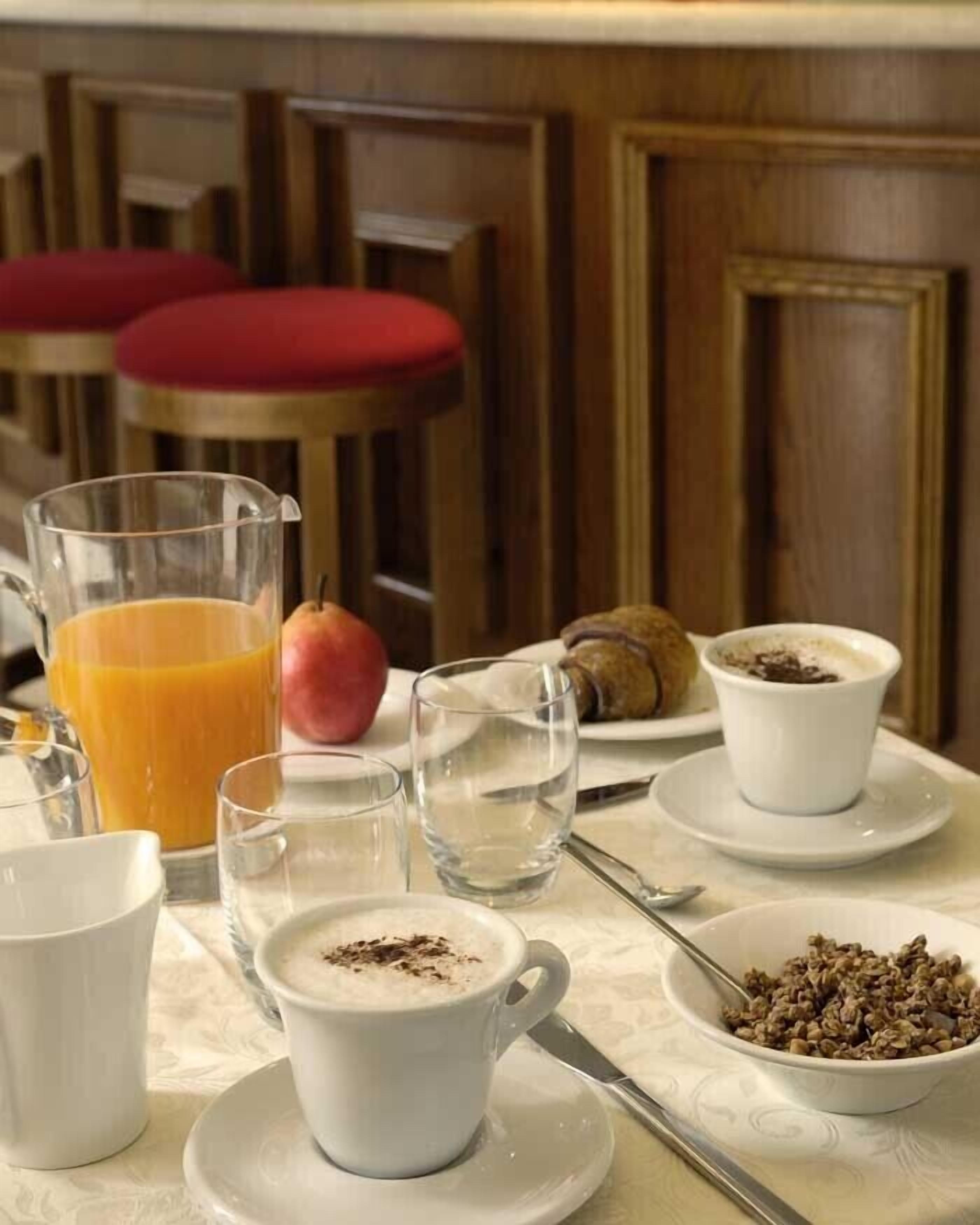 A breakfast table with a glass of orange juice, a plate of cereal, a croissant, and a cup of coffee.