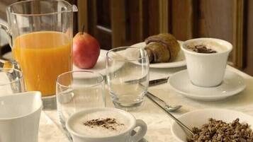 A breakfast table with a glass of orange juice, a plate of cereal, a croissant, and a cup of coffee.
