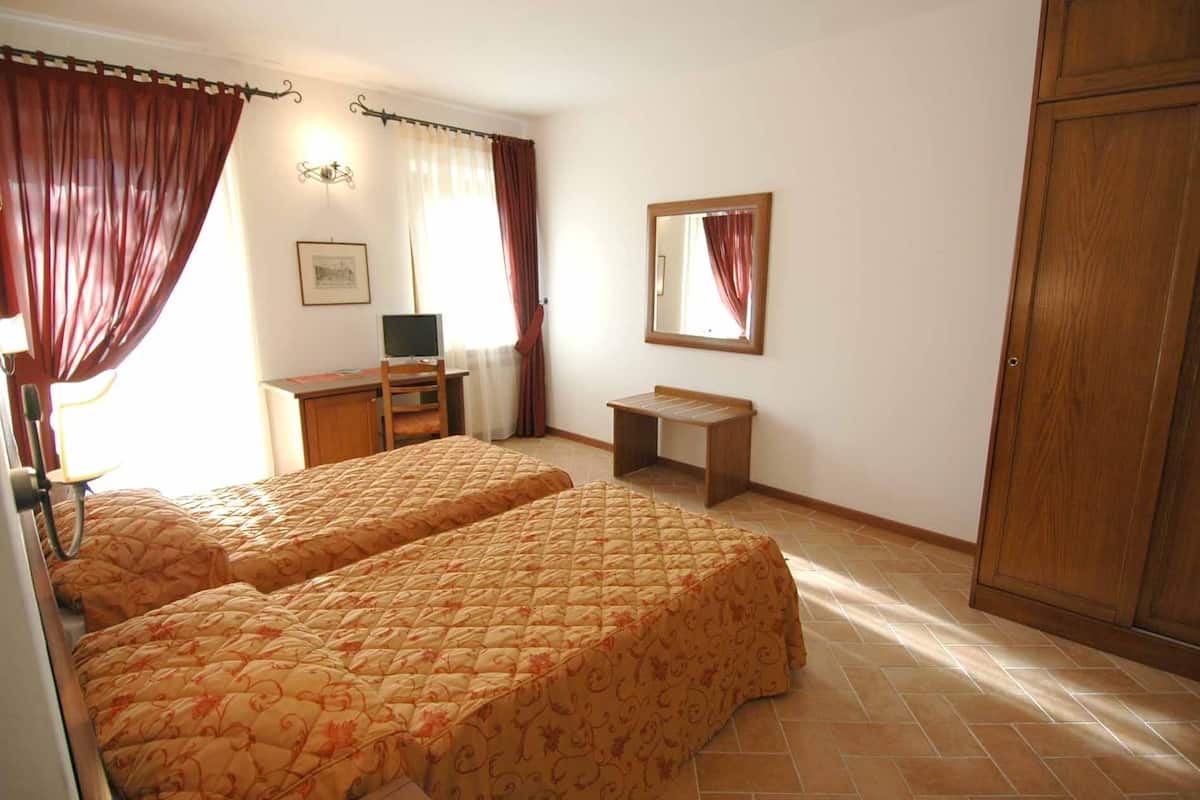 A bedroom with two beds, a desk, a chair, a wardrobe, and a mirror.