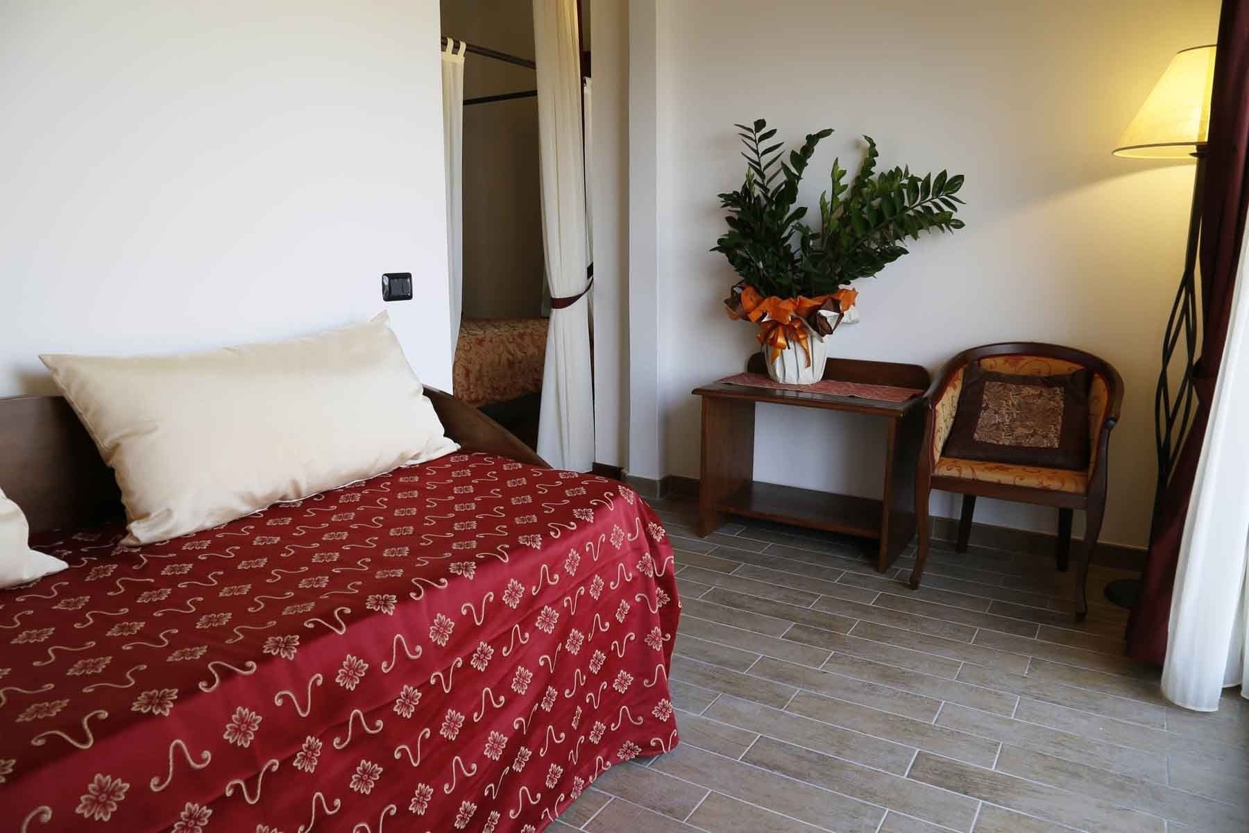A hotel room with a bed, a small table with a plant, a chair, and a lamp.