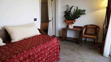 A hotel room with a bed, a small table with a plant, a chair, and a lamp.
