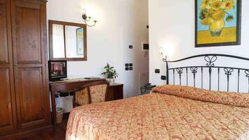 A hotel room with a bed, a desk with a chair, a wardrobe, and a painting on the wall.