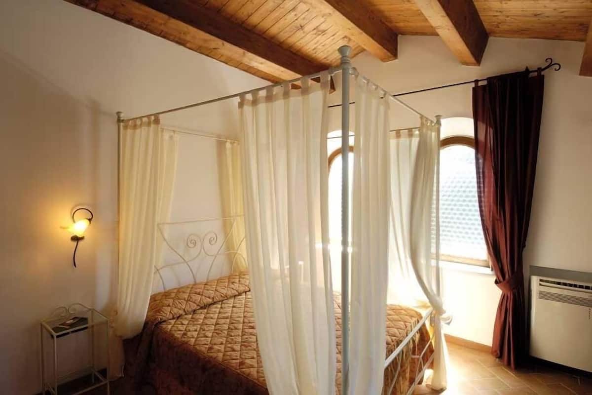 A room with a four-poster bed, a wall-mounted light, and a window with curtains.