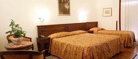 A hotel room with two beds, a nightstand with a telephone, a chair, a table with a vase, and a painting on the wall.