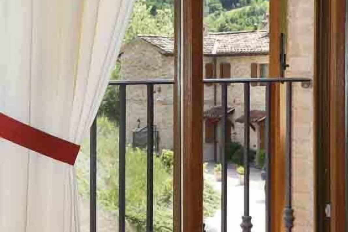 A room with a balcony overlooking a courtyard with traditional buildings and greenery.