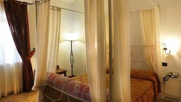 Un dormitorio con cama, cortinas, mesita de noche y lámpara.