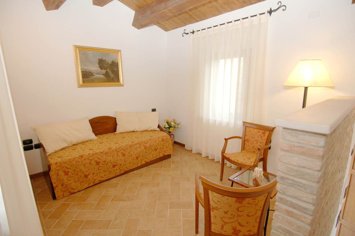 A bedroom with a bed, a chair, a lamp, a painting, and a window with curtains.