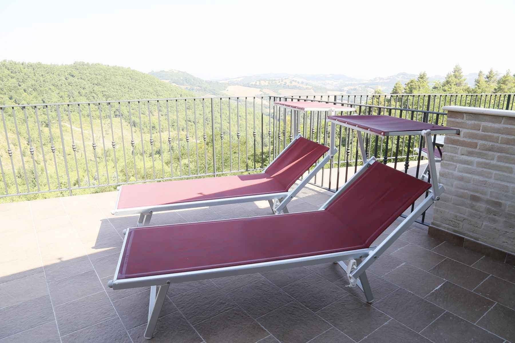 Two red lounge chairs on a balcony with a metal railing, overlooking a forested landscape.