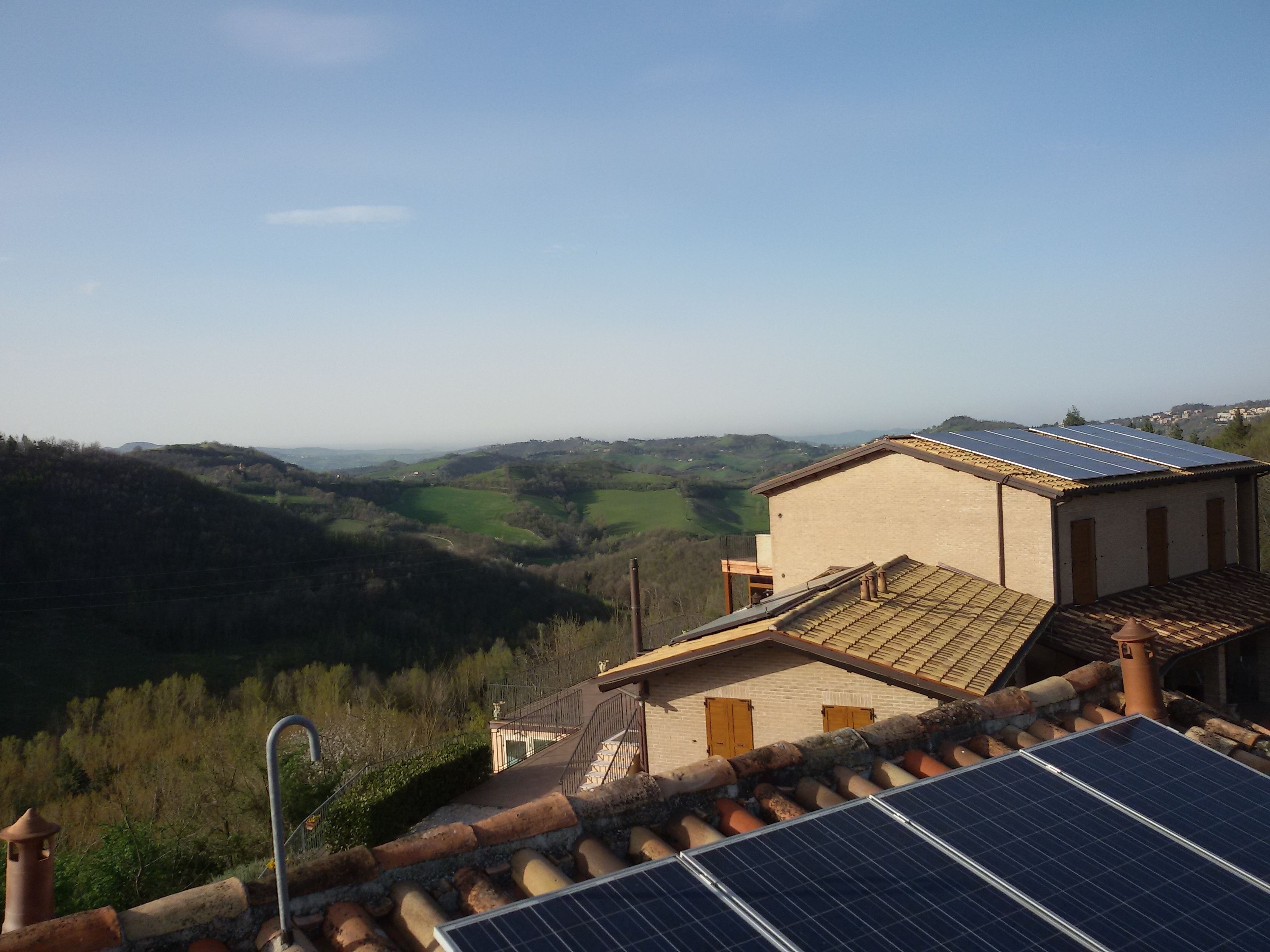 Ein Gebäude mit einem Ziegeldach und Solaranlagen, mit Blick auf ein Tal mit grünen Feldern und Hügeln.