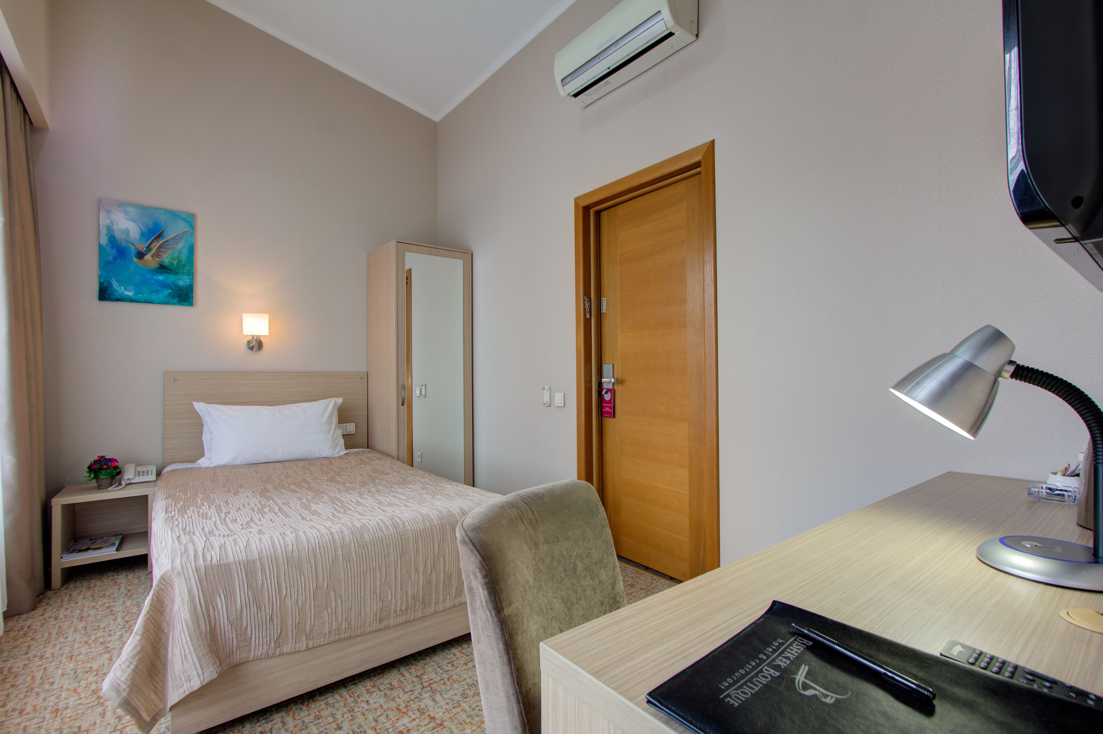 A hotel room with a bed, a desk, a chair, a lamp, a painting, and a door.