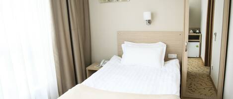 Habitación de hotel con una cama, una mesita de noche con teléfono, una lámpara de pared y un espejo que refleja la habitación.