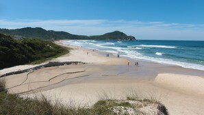 A beach with people walking along the shore, a sandy beach, and a view of the ocean. - Praia Hotel Imbituba (Imbituba)