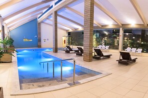 Una piscina interior con sillas de descanso, un jacuzzi pequeño y suelo de baldosas.