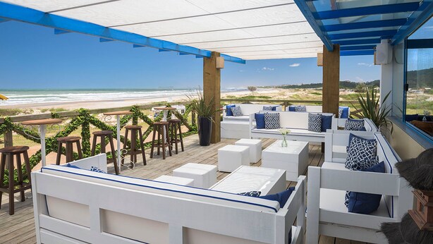 A beachside patio with white furniture, a glass ceiling, and a view of the ocean. - Praia Hotel Imbituba (Imbituba)
