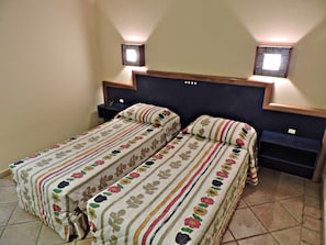 Un dormitorio con dos camas, cada una con ropa de cama estampada con motivos florales, cabeceros oscuros y dos mesitas de noche fijadas a la pared.