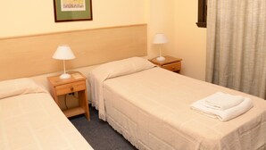 Una habitación de hotel con dos camas individuales, cada una con una mesita de noche de madera y una lámpara blanca. Encima de las camas hay un cuadro en la pared.