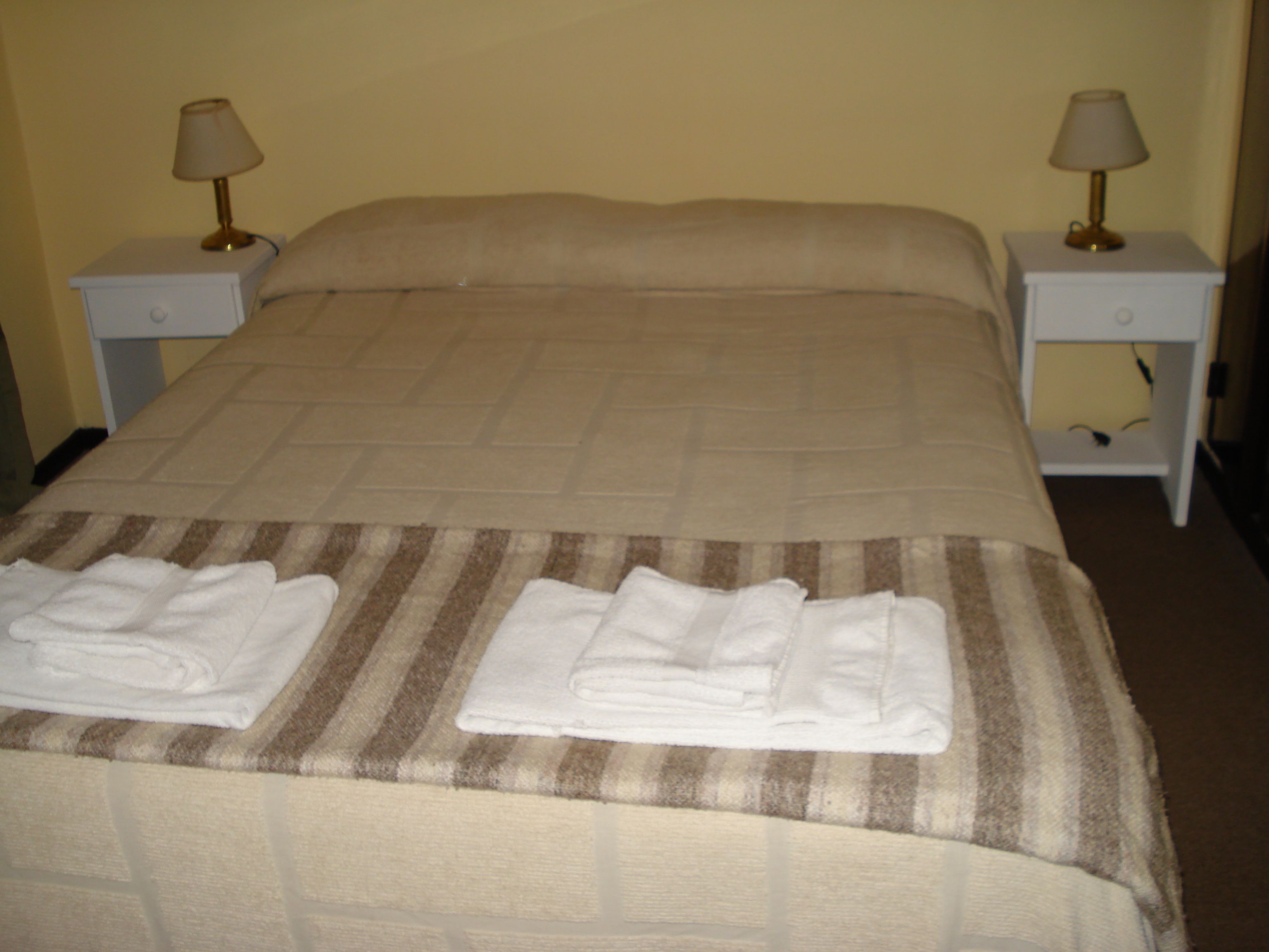 A neatly made bed with a striped blanket and two folded towels on the footboard. There are two bedside tables with lamps on either side of the bed.