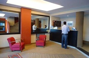 A hotel reception area with a counter, two red armchairs, and a large mirror reflecting the interior. - Hotel Mansilla (Mar del Plata)