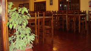 Un interior de restaurante con mesas y sillas de madera, ventiladores de techo y una planta en maceta.
