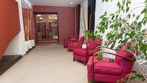 Un vestíbulo con piso alfombrado, un mostrador de recepción y tres sillones rojos con estructura de madera.