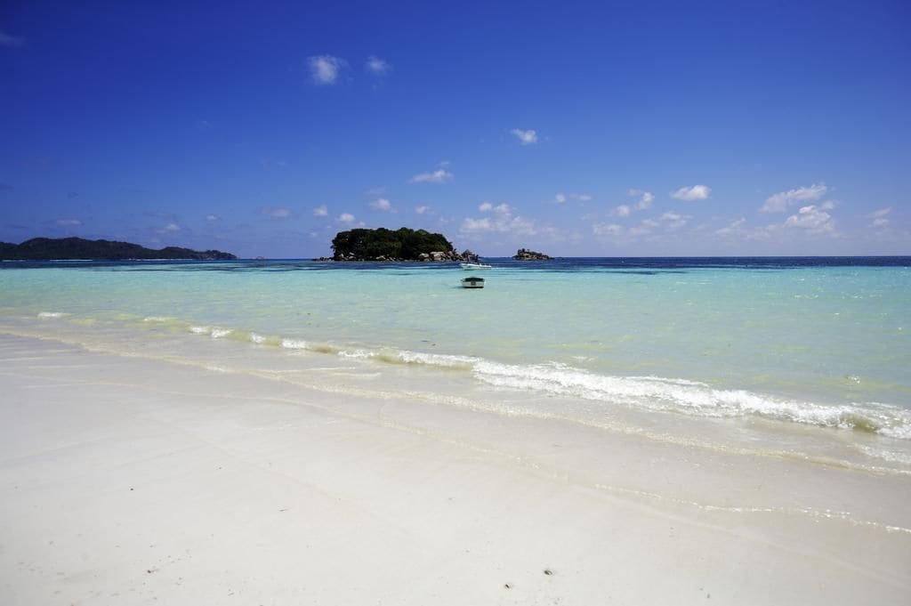 A beach with clear turquoise water, a sandy shore, and a small island in the distance.