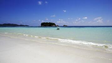 A beach with clear turquoise water, a sandy shore, and a small island in the distance.