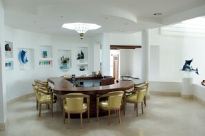 A spacious dining area with a round table surrounded by chairs, a kitchen area with a bar, and a view of the outdoors. - Village du Pecheur (Praslin Island)