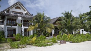 A two-story building with a thatched roof, surrounded by palm trees and a sandy beach. - Village du Pecheur (Praslin Island)