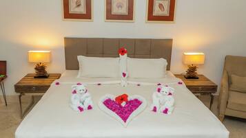 A neatly made bed with a heart-shaped flower arrangement and two white teddy bears.