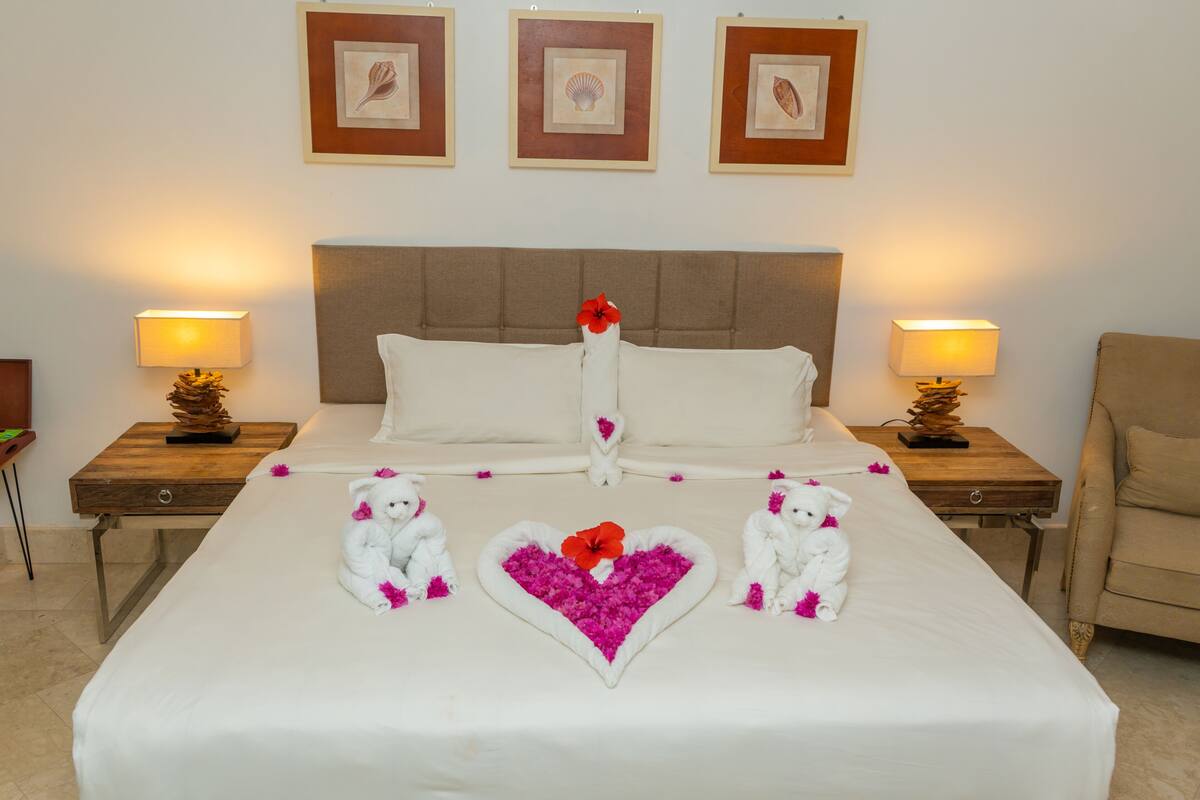 A neatly made bed with a heart-shaped flower arrangement and two white teddy bears.