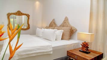 A hotel room with a bed, a nightstand, a lamp, a mirror, and a decorative plant.