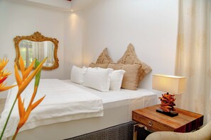 A hotel room with a bed, a nightstand, a lamp, a mirror, and a decorative plant. - Village du Pecheur (Praslin Island)